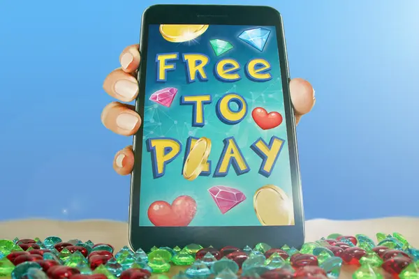 Eine Hand hält ein Smartphone mit der Aufschrift "FREE TO PLAY". Um die Schrift sind viele Münzen und Diamanten zu sehen, das Gerät steht auf einem Sandstrand mit Diamanten.