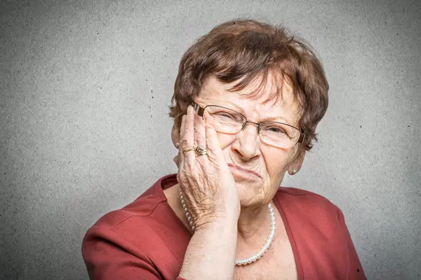Seniorin hält sich die Wange, weil ihr Zahnersatz Beschwerden verursacht.
