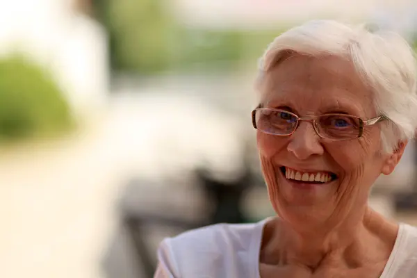 Seniorin lächelt zufrieden und zeigt dabei ihre schönen dritten Zähne (Zahnersatz).