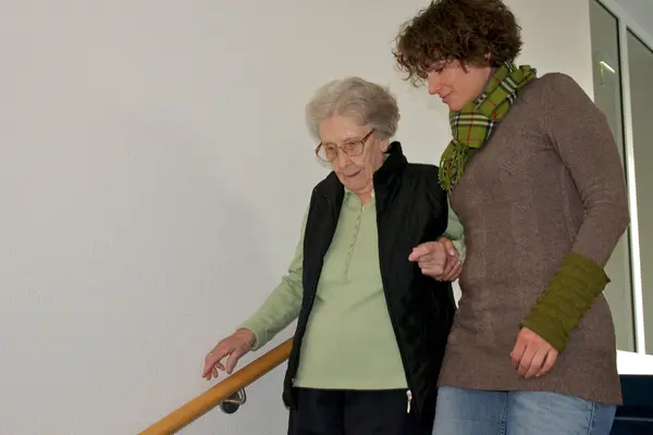 Eine junge Frau hilft einer älteren die Treppe hinab.