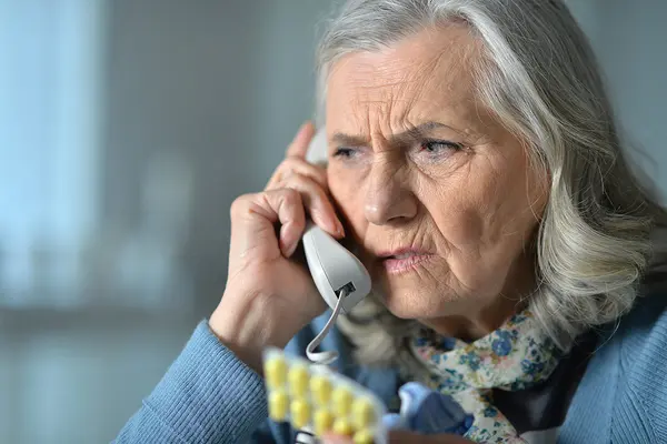 Ätere Dame hört am Telefonhörer kritisch zu