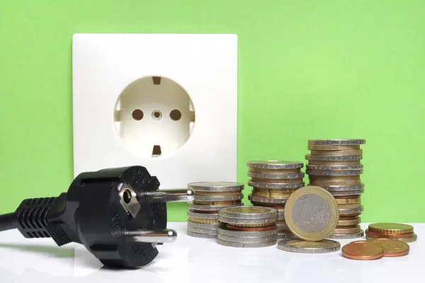 Stromstecker und Münzen liegen vor einer Steckdose