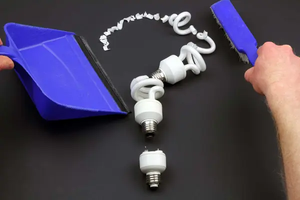 Zerbrochene Lampen als Fragezeichen aufgereiht, Hand mit Handfeger daneben