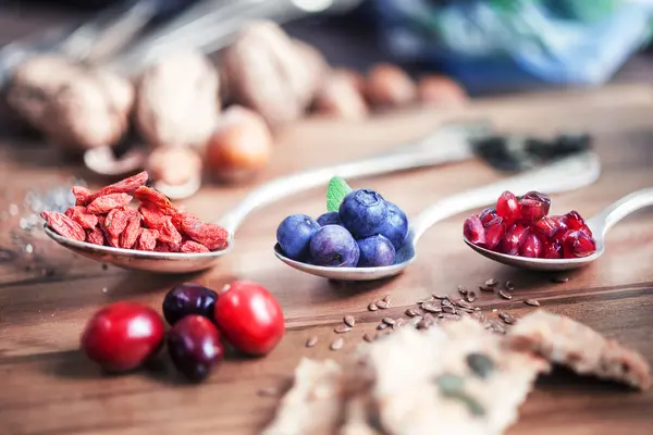 Goji Beeren, Acai Berren und andere sogenannte Superfoods liegen in einem Löffel auf einer hölzernen Arbeitsplatte