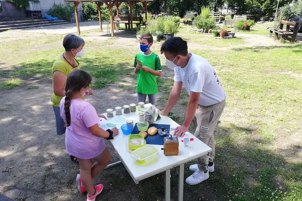 Drei Kinder und eine Erwachsene stehen an einem Tisch mit verschiedenen Materialien.