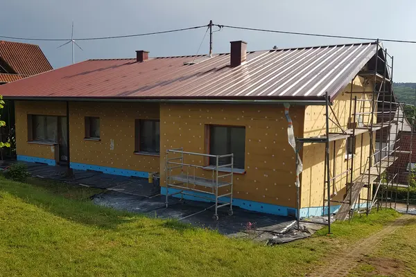 Ein einstöckiges Haus wird saniert. Wärmedämmplatten werden außen am Haus angebracht. Verschiedene Baugerüste sind zu sehen.