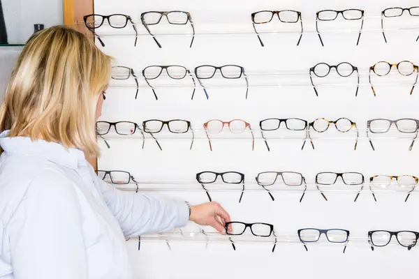 Eine Frau steht beim Optiker vor einer großen Auswahl an Brillen.