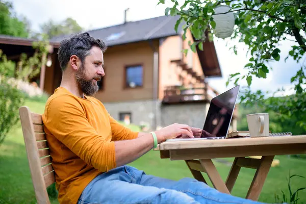 Mann sitzt im Garten am Laptop.
