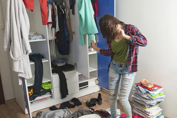 Junge Frau tanzt vor ihrem Kleiderschrank. Drumherum liegen lauter Kleidungsstücke.