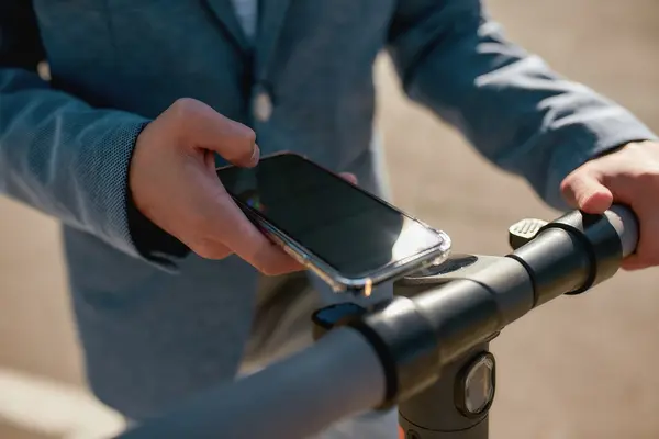 Eine Person hält sein Smartphone an einen E-Roller.