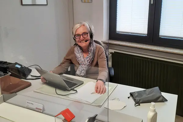 Eine Frau sitzt an einem Bürotisch und lächelt in die Kamera.