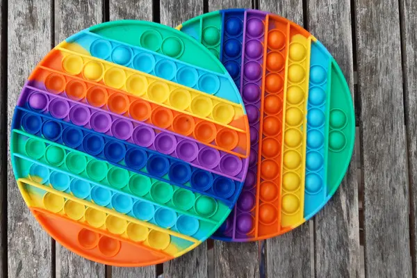 Zwei runde, bunte Pop-it-Fidget-Toys liegen auf einem Holztisch