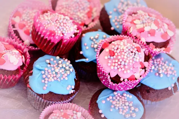 Muffins mit buntem Zuckerguss und Zuckerstreuseln auf einem Tisch.