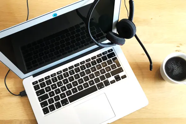 Ein Laptop mit Kopfhörern und eine Kaffeetasse stehen auf einem Tisch.