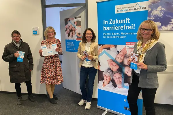 Vier Frauen stehen vor einem Plakat und lachen in die Kamera. Der Anlass ist die Wiedereröffnung der Landesberatungsstelle in Ingelheim 