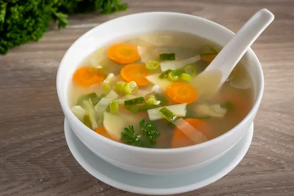 Ein Suppenteller mit einer Gemüsesuppe. Ein Löffel liegt bereits im Suppenteller.