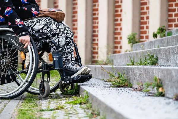 Eine Person im Rollstuhl steht vor einer Treppe und kann nicht weiter fahren.