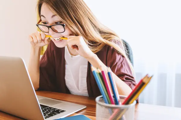 Eine Frau sitzt vor dem Laptop und beißt verzweifelt auf einen Bleistift.