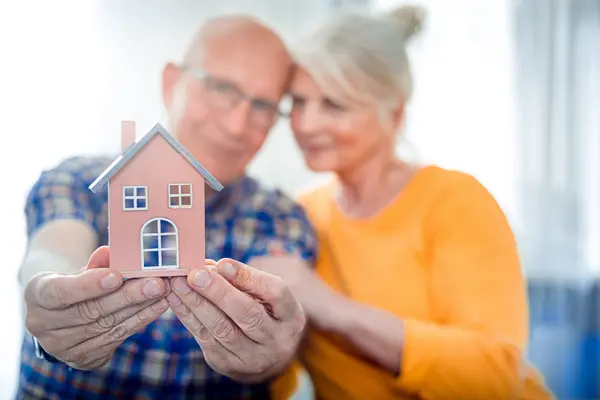 Älteres Ehepaar halten ein kleines Haus in den Händen