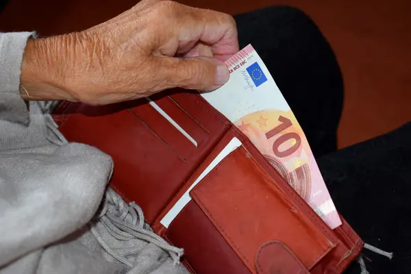 Hand einer älteren Frau zieht einen 10 Euro-Schein aus einem Geldbeutel.