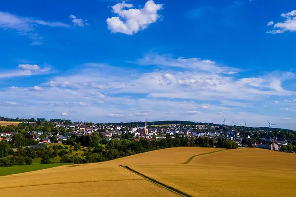 Ein weites Feld mit einem Ort im Hintergrund und blauem Himmel.