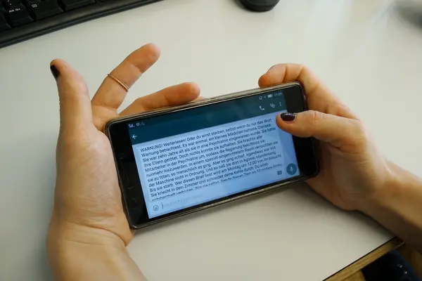 Eine Frau hält ein Handy in der Hand uns liest einen Kettenbrief.