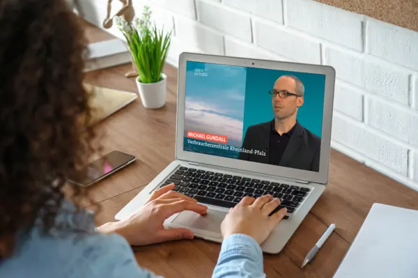 Eine Frau an einem Laptop. Auf dem Bildschirm ist ein Mann zu sehen, der gerade etwas erklärt.