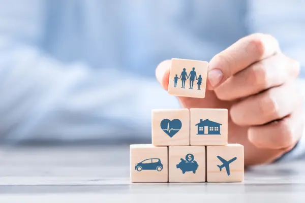 Würfel mit verschiedenen Symbolen (Auto, Sparschwein, Herz, Haus, Flugzeug, Familie) werden zu einer Pyramide gestapelt