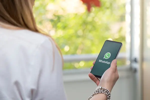 Eine Frau hält ihr Smartphone in der Hand. Auf dem Display ist das Logo von WhatsApp zu sehen. 