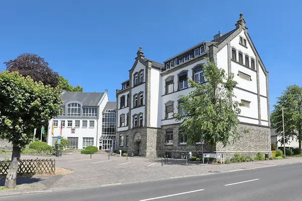 Ein Gebäude. Davor ein großer Platz mit einem Baum.