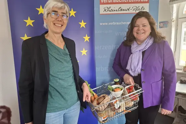 Zwei Frauen vor einem Roll-up mit der Europafahne. Sie halten einen Einkaufskorb zwischen sich.
