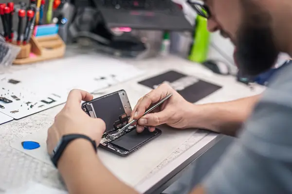 Ein Mann repariert ein Smartphone an einem Werkstatttisch.