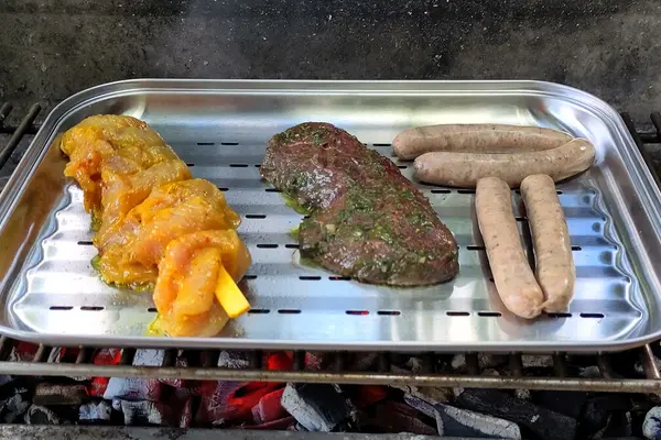In einer Aluschalen liegen ein Spieß, ein Stück Grillfleisch und Grillwürstchen.