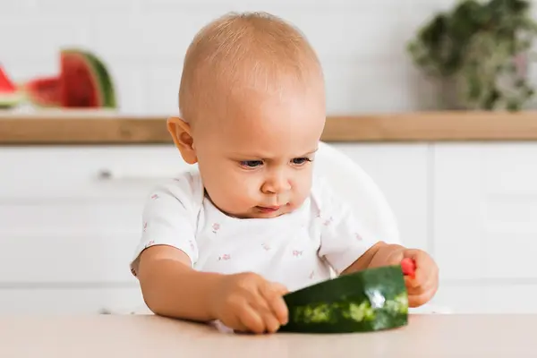 Ein Kleinkind betrachtet und befühlt ein Stück Wassermelone