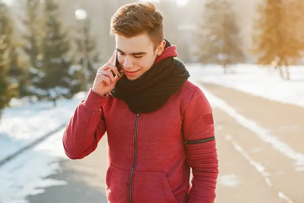 Ein Junger Mann trägt eine rote Fleecejacke. Er läuft auf einer winterlichen Straße und telefoniert.  