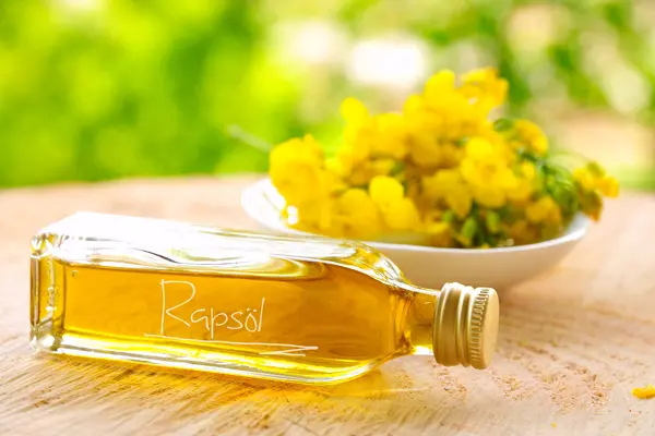 Eine Flasche Rapsöl liegt vor einer Schale mit Rapsblüten.