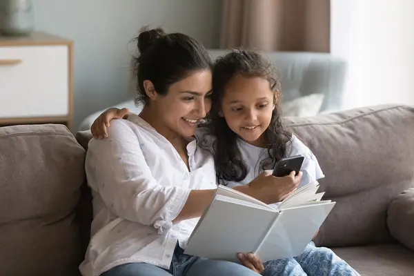 Mutter und Kind sitzen gemeinsam auf der Couch und schauen auf einen Smartphone.