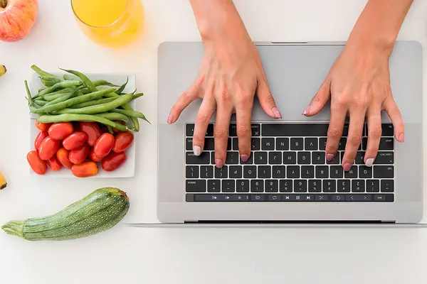 Hände auf einer Laoptoptastatur, Gemüse und Früchte
