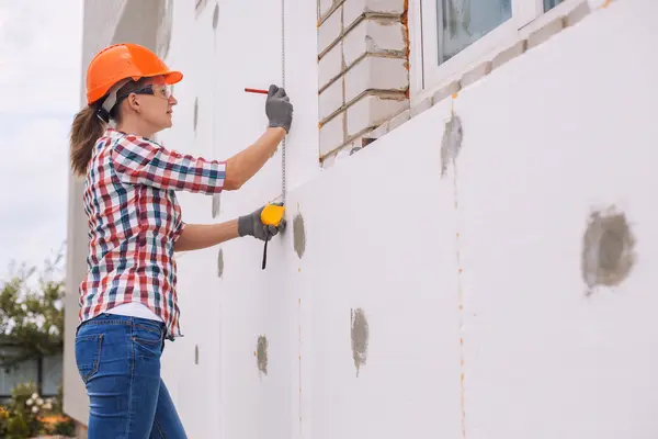 Frau in Arbeitskleidung dämmt Hausfassade