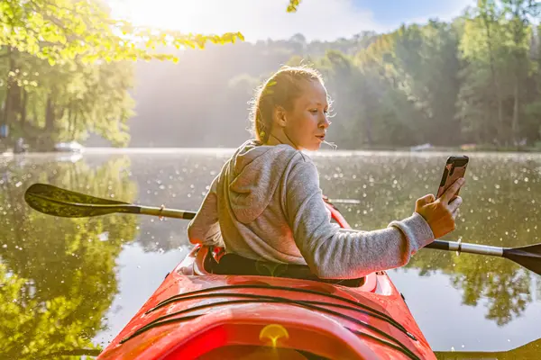 Frau sitzt in einem Paddelboot und macht ein Foto