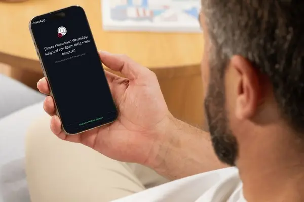 Ein Mann hält ein Smartphone in der Hand, auf dessen Disyplay in weißer Schrift auf schwarzem Hintergrund steht: "Dieses Konto kann WhatsApp aufgrund von Spam nicht mehr benutzen. Chats sind noch auf diesem Gerät."