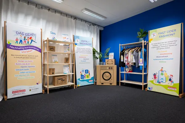 Die Wanderausstellung "Das geht! Nachhaltig konsumieren und leben" mit den drei Bannern, einem Regal und einem Kleiderständer 