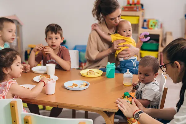 Kinder unterschiedlichen Alters sitzen mit zwei Betreuerinnen am Esstisch