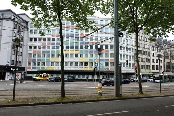 Ansicht eines mehrstöckigen Gebäudes mit farbiger Gestaltung der Frontseite, Straße mit Straßenbahngleisen, ein parkender Krankenwagen