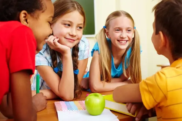 4 schüler sitzen am tisch und lächeln, ein Apel liegt auf dem Tisch