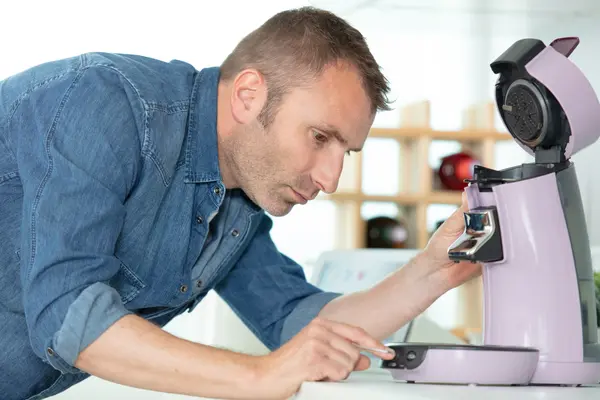 Mann drückt Knopf auf kaputter Kaffeemaschine
