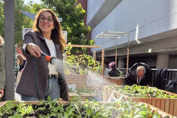 Frau gießt mit einem Schlauch lachend ein Hochbeet