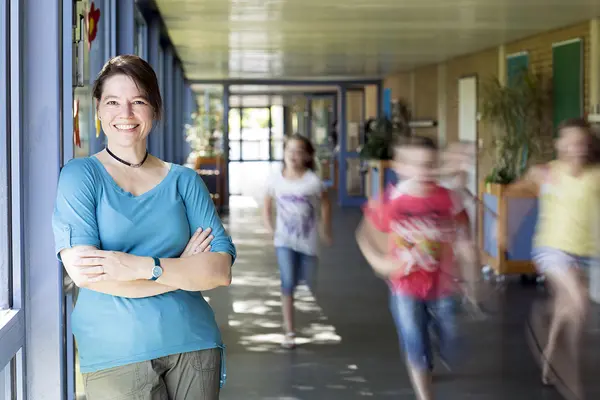 Eine Lehrkraft steht im Flur eines Schulgebäudes, Kinder rennen vorbei