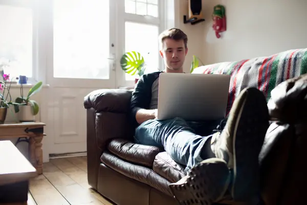 Junger Mann sitzt auf der Couch an seinem Laptop