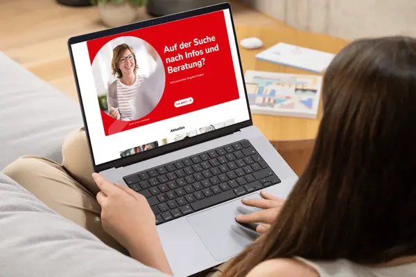 Frau liegt auf einem Sofa mit Laptop auf dem Schoß, auf dem Display die Internetseite verbraucherzentrale.nrw: Logo der Verbraucherzentrale Nordrhein-Westfalen, Text: "Auf der Suche nach Infos und Beratung? Jetzt passendes Angebot finden! Los geht's", eine lächelnde Frau die an der Kamera vorbei einen anderen Menschen ansieht.